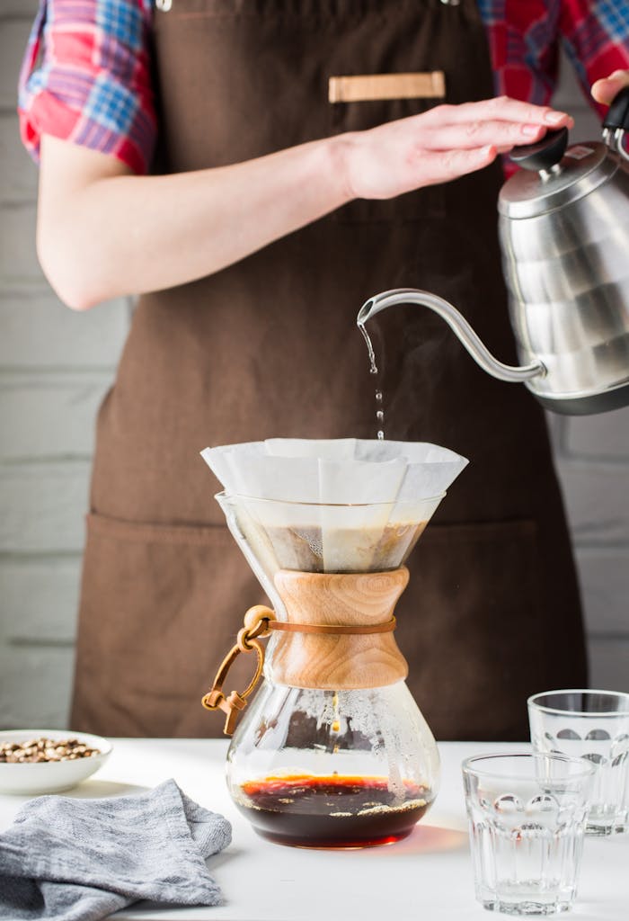 Barista pours hot water into Chemex for fresh drip coffee. Perfect for caffeine lovers.